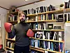 Mann står foran ei bokhylle med mange bøker. Han har på seg røde boksehansker og ser tenkende ut i lufta