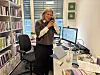 Kvinne står foran skrivepult med PC og snakker i telefonen