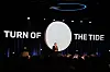 Foredragsholder på scenen foran teksten «TURN OF THE TIDE» og et stort rundt lerret.