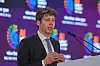 Sam Altman taler ved talerstol under AI Summit i New Delhi med lysende skjerm bak seg.