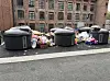 Overfylte avfallscontainere med søppelposer foran en murbygning