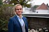Mann i blå dress står på takterrasse med hus og trær i bakgrunnen
