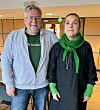 To personer står i en foaje med lys vegg, døråpninger og tregulv.