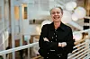 Smilende person i svart antrekk står med armene i kors i et lyst kontorinteriør.