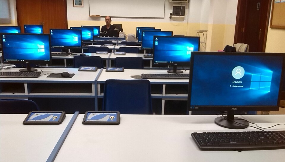 Et klasserom med lærer, men ingen elever. Mange skjermer som er skrudd på.
