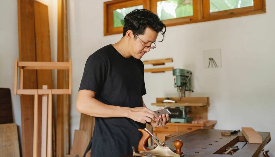 En ung mann med briller og T-skjorte justerer en gammeldags høvel.