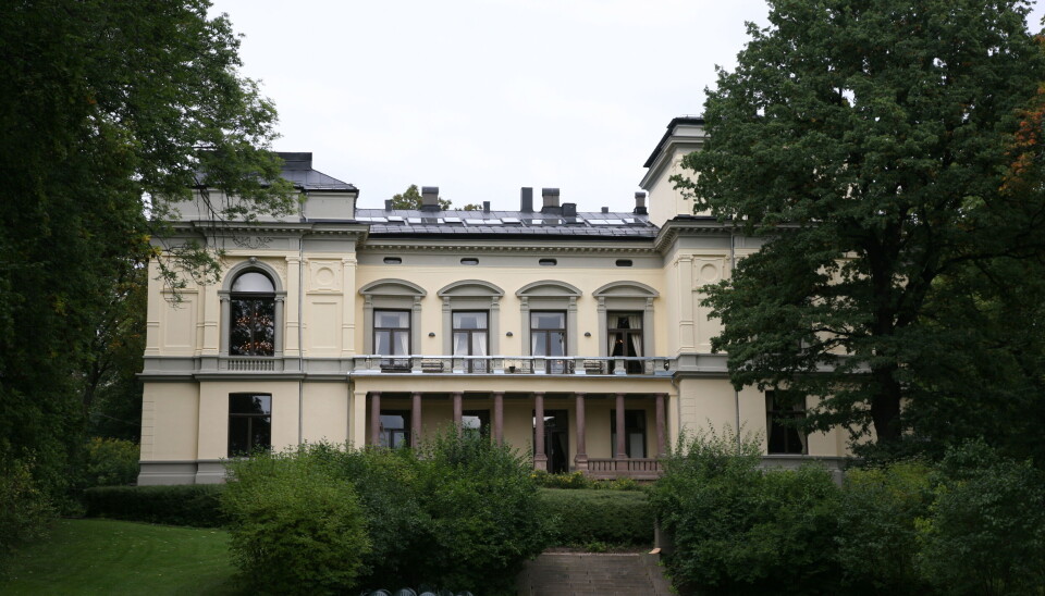 Her se vi en staselig bygning som ligner litt på et slott. Foran er det en vakker hage og store trær.