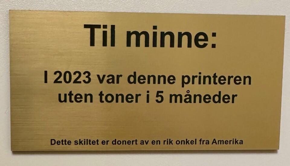 Et gullskilt der det står 'Til minne: i 2023 var denne printeren uten toner i 5 måneder', som henger på en printer på Oslomet.