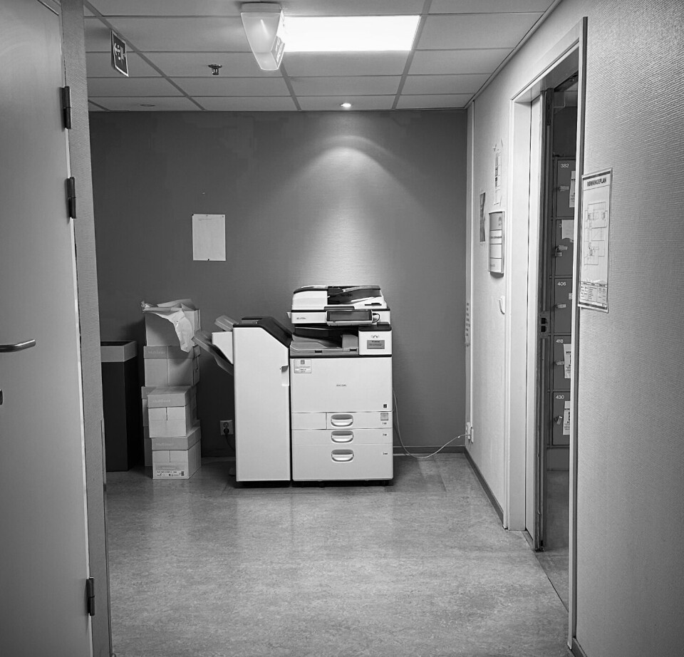 Et svart-hvitt bilde av en printer i en lang korridor.