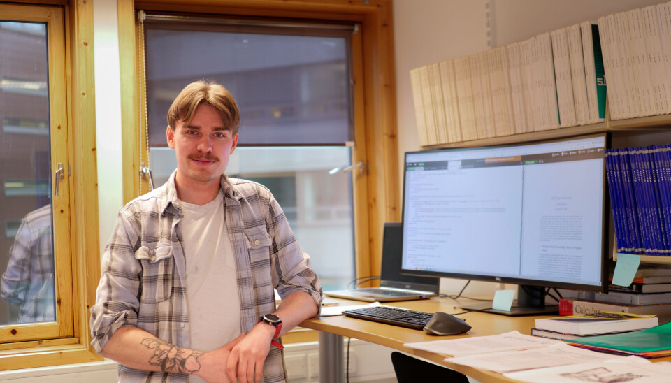 En smilende blond mann med bart står foran en pc-monitor på et kontor. Det er Sondre Bolland.