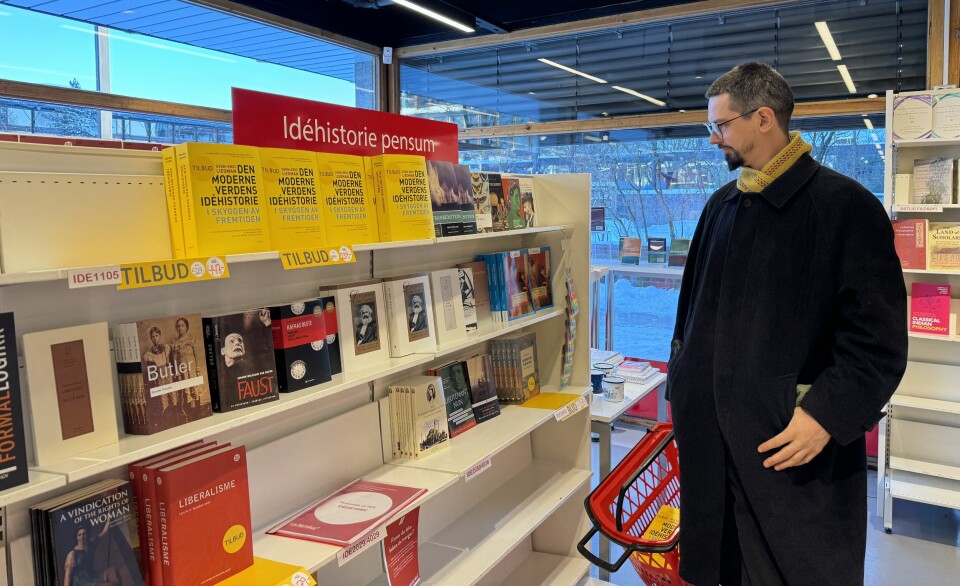 En høy mann i svart vinterfrakk står og ser på en bokhylle i en butikk. Det er en lapp på toppen av hylla der det står 'Idehistorie pensum'.