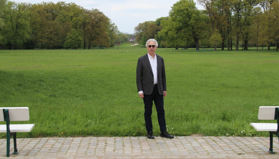 Mann i hvit skjorte og blazer står i et stort parkanlegg