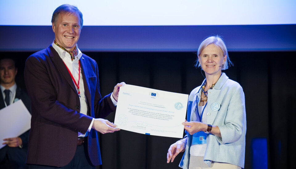 Gediminas Karoblis mottar pris på vegne av NTNU for godt samarbeid i Erasmus Mundus-programmet. Til høyre er Sophie Beernaerts, direktør ved European Education and Culture Executive Agency (EACEA). En smilende mann og en smilende dame holder sammen et stort ark/diplom. I bakgrunnen er en scene. Prisutdeling.