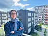 Portrett av Hamideh Kaffash. Vi ser en ung kvinne med hijab, som står foran tre blokker i grått.